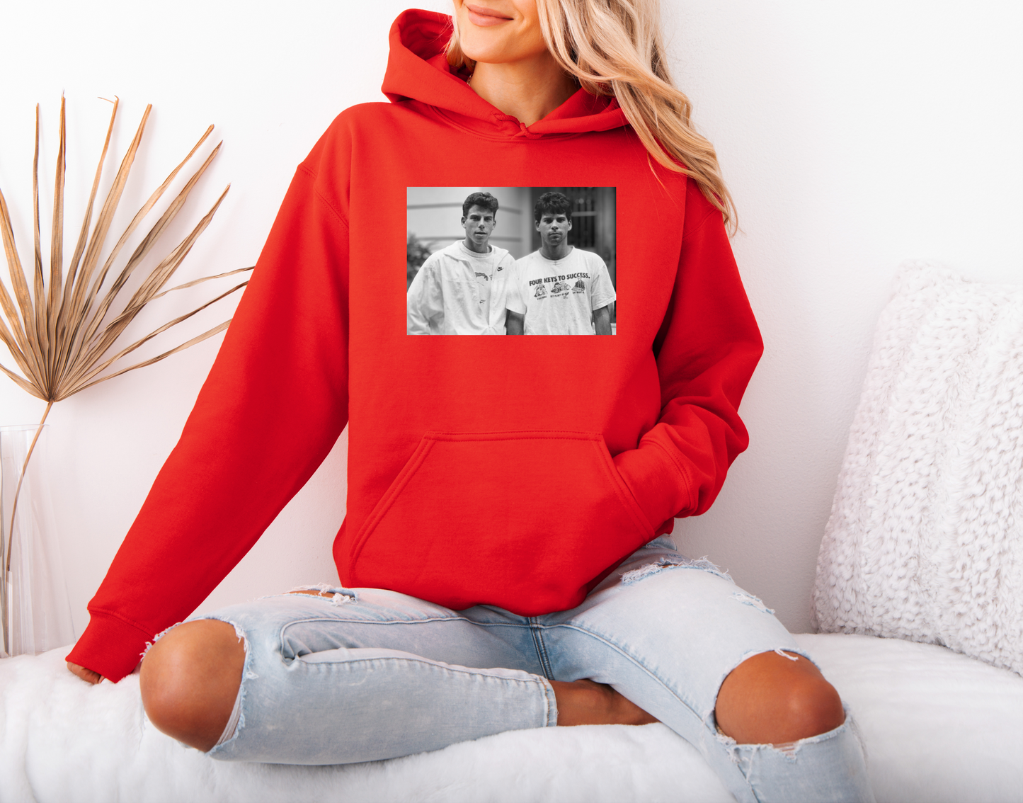 a woman sitting on a bed wearing a red hoodie
