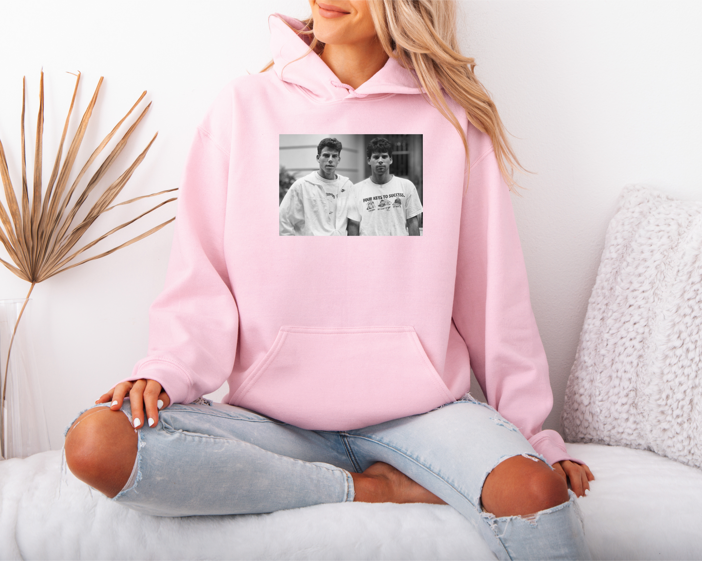 a woman sitting on a bed wearing a pink hoodie