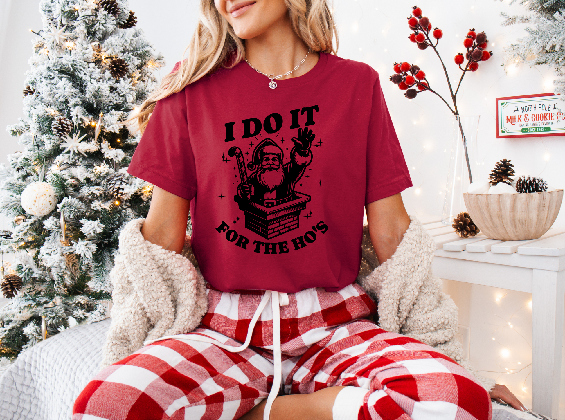 a woman sitting on a bed wearing a red shirt and plaid pants