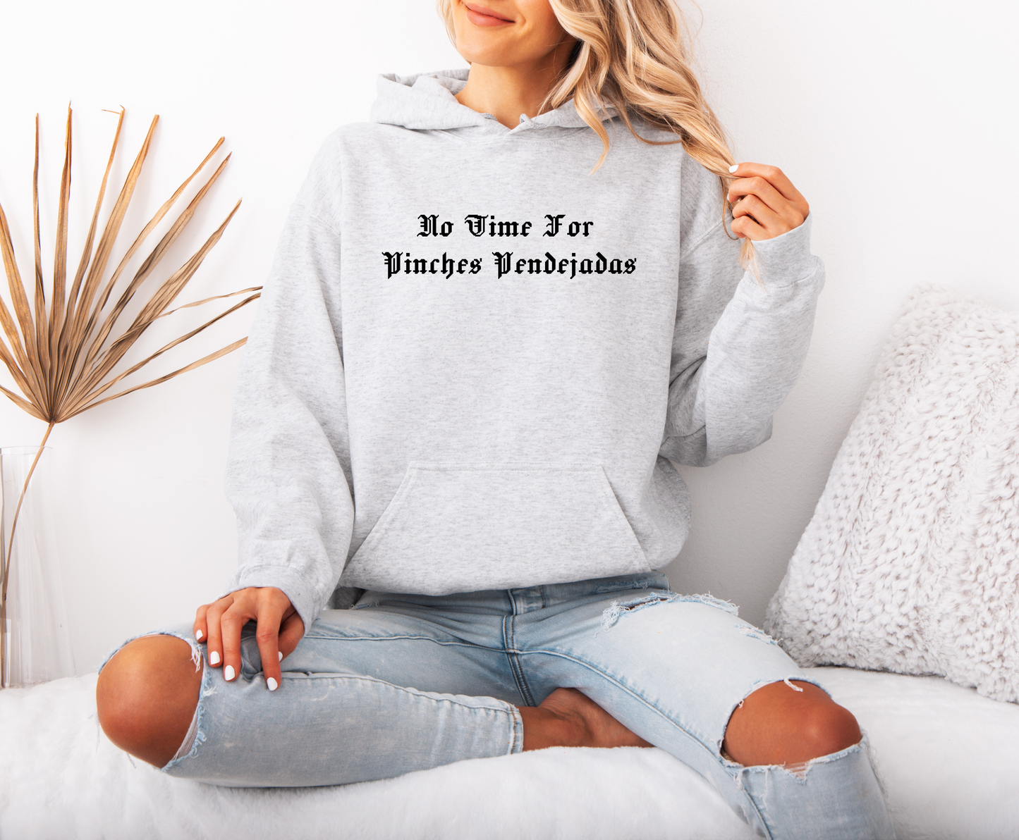 a woman sitting on a bed wearing a grey hoodie